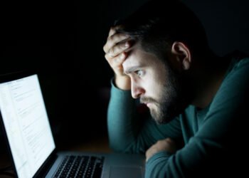 Homem cansado olhando para a tela do notebook, ilustrando os impactos da fadiga da cibersegurança no ambiente digital.