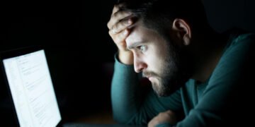 Homem cansado olhando para a tela do notebook, ilustrando os impactos da fadiga da cibersegurança no ambiente digital.