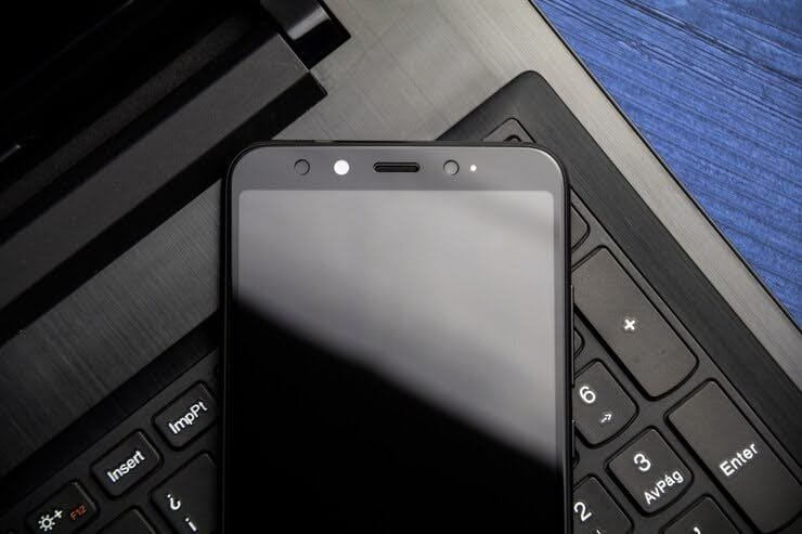 Smartphone com a tela desligada sobre o teclado de um notebook preto.